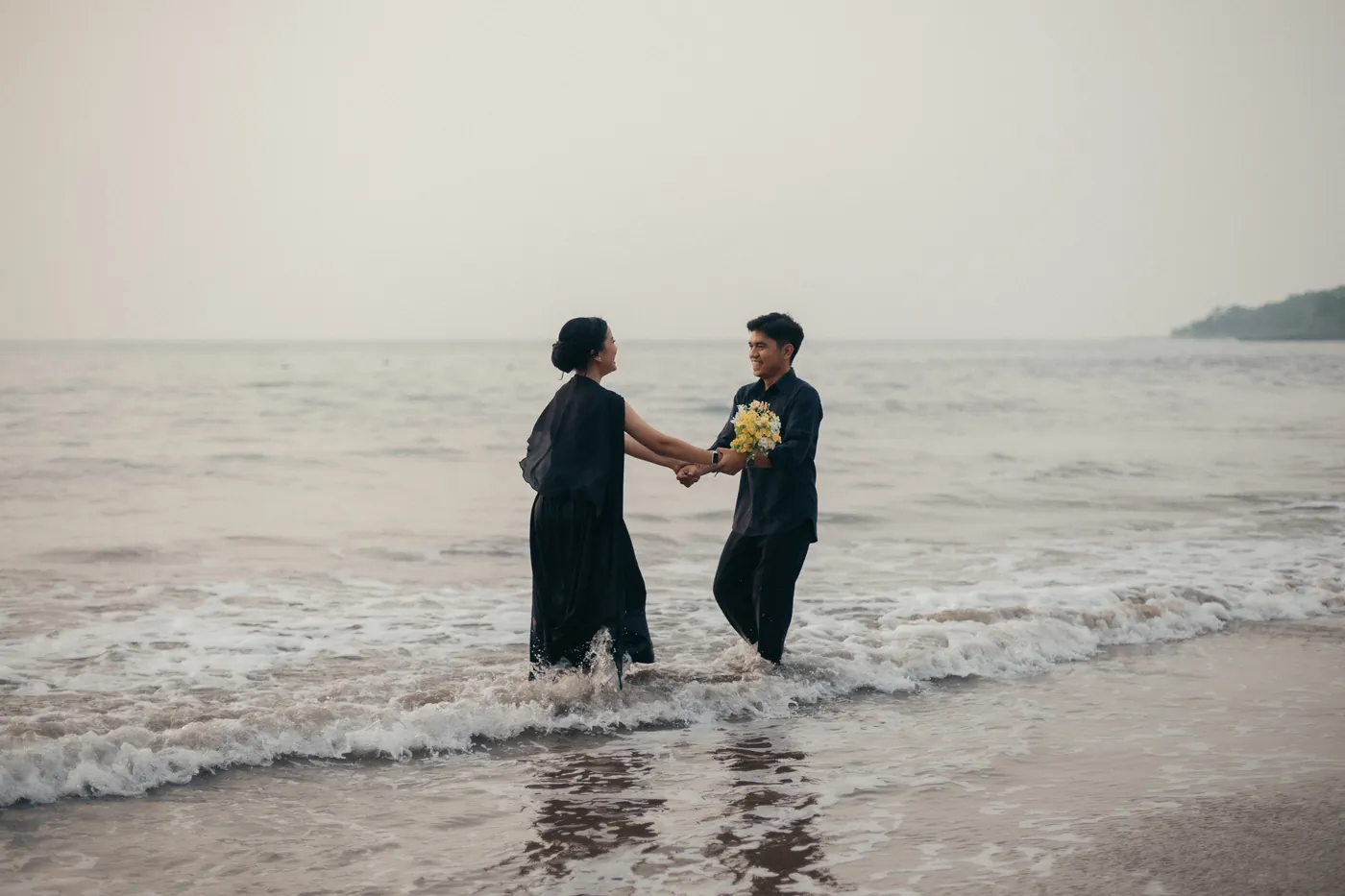 Bastian and Vero holding hands in the waves at the beach