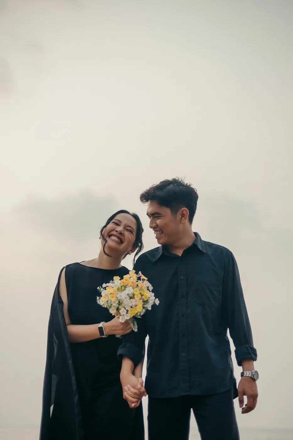 Bastian and Vero laughing together, holding hands and a bouquet of yellow and white flowers